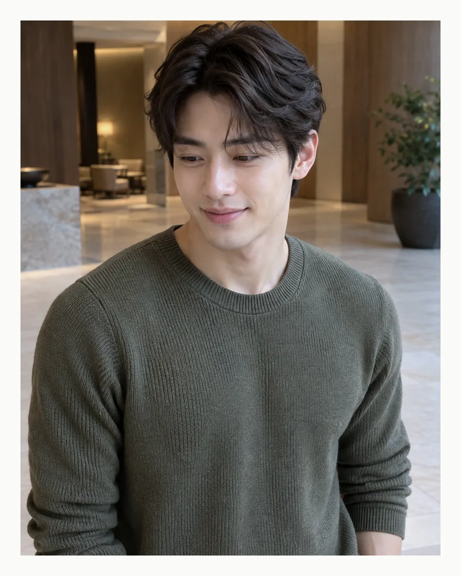 흰 여백 안 따뜻한 조명의 로비에서 올리브 니트 차림으로 미소 짓는 모습